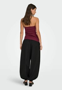 Bordo oprijet top s nabranimi detajli, v kombinaciji s širokimi črnimi hlačami, ki imajo elastične manšete in širok kroj. Črne čevlje na blok peto.