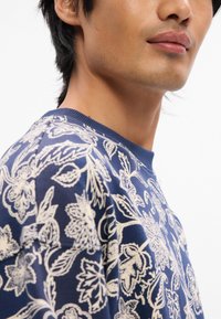 Μπλέ ναυτικού φούτερ με λουλουδάτο σχέδιο σε κρεμ απόχρωση, στρογγυλή λαιμόκο ψη και υφή υφάσματος. Ορατές ραφές κατά μήκος των ραφών.