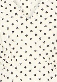 Robe crème à pois noirs irréguliers, col en V et taille froncée.