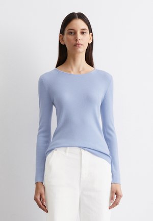 Ribbed light blue long-sleeve top with a round neckline, worn with white pants. Smooth texture, fitted design, with subtle stretch.