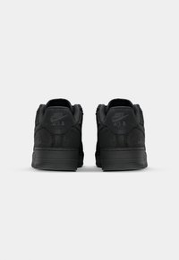 Sapatilhas Nike Air pretas com um upper liso, acentos texturizados, sola de borracha e marcação em relevo no calcanhar.