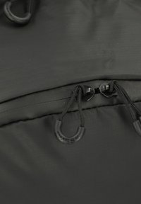 Sac à dos en tissu noir avec une texture lisse, fermeture à cordon, et une poche zippée avec des accessoires en noir et un logo.