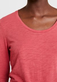 Rosarosa långärmad t-shirt med rund halsringning, tillverkad av ett mjukt, texturerat tyg, som visar en avslappnad passform och släta sömmdetaljer.