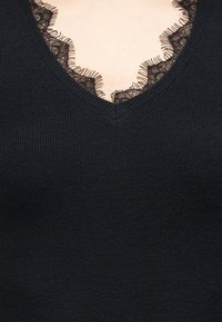 Μαύρο μπλουζάκι με ραβδωτό πλεκτό ύφασμα και V-λαιμόκοψη, με λεπτή μαύρη δαντέλα κατά μήκος του λαιμού, που αφήνει να φανεί μικρό τμήμα δέρματος από κάτω.