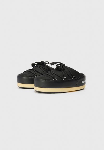 Chaussures noires avec une semelle ronde et surélevée, dotées d'un dessus en tissu doux, présentant des lacets décoratifs et une semelle beige contrastante.