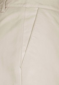 Tessuto in pelle beige con una texture liscia, caratterizzato da una cucitura diagonale e dettagli di cucitura a contrasto.