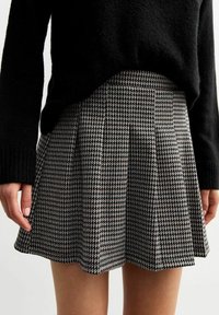 Falda plisada de estampado de pata de gallo en blanco y negro, hecha de un tejido texturizado, con un diseño acampanado y un dobladillo que se sitúa por encima de la rodilla.