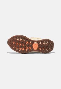 Löparskosula med ett robust, strukturerat mönster. Har en brun gummibas med orange detaljer och framträdande dubbar för grepp.