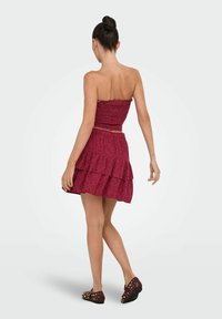 Bordeaux tweed twee-delige outfit met een gesmokt tube-top en een gelaagde rok. De stof heeft een bloemenpatroon en is gecombineerd met versierde platte schoenen.
