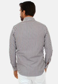 Camicia a righe marrone e bianca con maniche lunghe, polsini abbottonati e colletto classico. Realizzata in un tessuto morbido con una vestibilità sartoriale.
