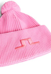 Caciula tricotată roz cu o textură cordonată, având un pom-pom rotund în partea de sus și un logo brodat într-o nuanță mai deschisă de roz pe margine.