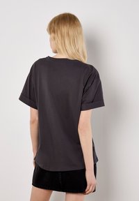 Graues T-Shirt mit kurzen Ärmeln und lockerer Passform, aus weichem Baumwollmaterial und mit umgeschlagenen Ärmeln, von hinten betrachtet.