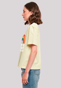Light yellow cotton t-shirt with a loose fit, featuring a rainbow graphic and white text on the front, short sleeves, and a straight hem.