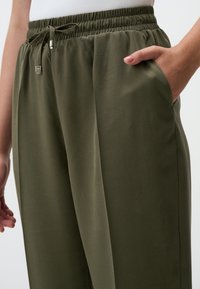 Pantalons ajustés légers couleur vert olive avec une taille élastique, cordon de serrage et poches latérales. Texture lisse et coupe ample.
