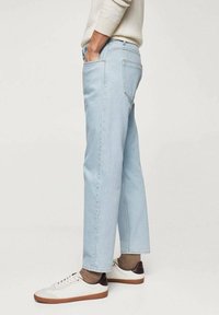 Jeans de un azul claro con un ajuste relajado, cinco bolsillos y costuras en contraste. Llevados con zapatillas blancas con detalles en marrón.