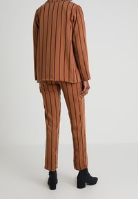 Braun gestreifter Blazer und Hosenanzug aus glattem Stoff; mit vertikalen marineblauen Streifen, taillierter Passform und klobigen schwarzen Heels.