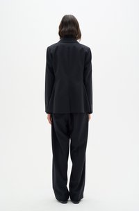 Black tailored suit jacket with a single vent, paired with loose-fitting black trousers, both crafted from smooth fabric.