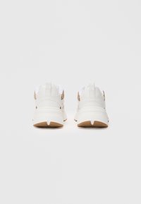O pereche de sneakers albi și bej văzuți din spate, cu tălpi late și mânere pentru tragere, pe un fundal alb simplu.