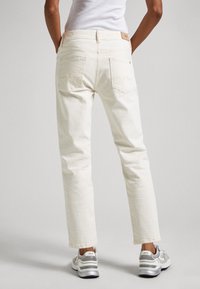 Vita denimjeans med rak passform och medelhög midja. Har två bakfickor och ett brunt läderbadge från märket. Bärs med grå sneakers.