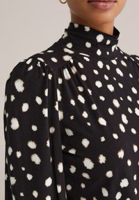 Czarna bluzka z białym i brązowym wzorem w cętki, z wysokim kołnierzem, plisowanymi ramionami i miękką fakturą. Posiada luźny krój z subtelnymi detalami.