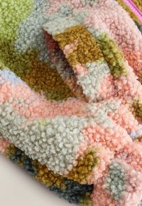 Mjuk, krullig ulltyg med texturerade öglor i pastellrosa, grönt, senapsgult och grått abstrakt mönster, vikt på ljus yta.