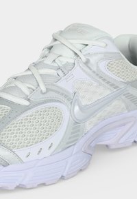 Λευκό και ανοιχτό γκρι παπούτσι τρεξίματος Nike με πλέγμα, λογότυπο Swoosh στο πλάι, επενδυμένο γιακά και παχιά υφή στη σόλα.