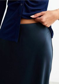 Marineblaues Oberteil mit Knopfverschluss und gerafftem Detail, kombiniert mit einem glatten, dunkelgrünen, figurbetonten Rock.