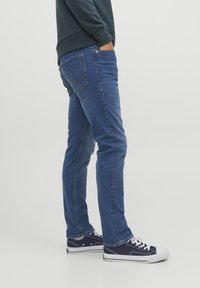 Jeans in denim di un blu scuro, a taglio slim con dettagli di cucitura discreti. Indossati con sneaker blu navy, che mostrano uno stile casual.
