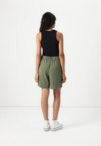 Haut sans manches noir et shorts verts olive avec taille élastique. Baskets montantes blanches. Coupe simple et décontractée.