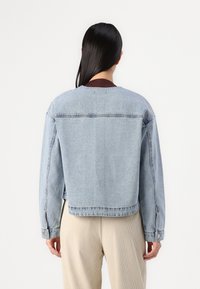 Svetlo modra jeans jakna z ohlapnim krojem, ki ima dolge rokave, okroglo področje vratu in vidne šive ob šivih.