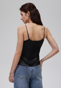Svart sateng camisole med tynne stropper, med en glatt tekstur og en tettsittende design, båret med høytlivs blå denimjeans.