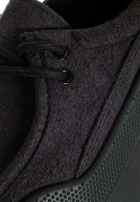 Scarpa nera con texture, tomaia effetto feltro, con lacci neri e occhielli, e suola robusta in gomma nera con motivo a puntini.