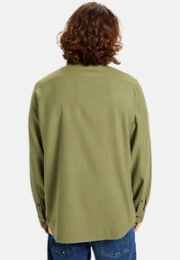 Camisa de manga larga en color verde oliva, hecha de una tela suave, con puños abotonados y dobladillo redondeado. La vista trasera muestra un corte relajado y una textura suave.