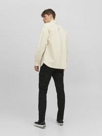 Cream button-up shirt with a pointed collar, paired with black cargo pants. Texture appears smooth; model wearing black sneakers.