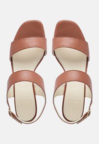 Sandali in pelle marrone con due ampie cinghie, design aperto davanti e fibbia alla caviglia. Superficie liscia con una soletta chiara e un marchio.
