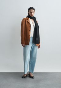 Brūns zamšs bleizeris, balts topiņš ar aukliņu detaļām, gaiši zili džinsi, melna ribota šalle un melni plakanie apavi ar caurspīdīgu detaļu.