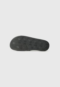 Semelle de chaussure noire avec une surface texturée présentant des motifs hexagonaux et des rainures pour l'adhérence. Design plat sans marques ni accents visibles.