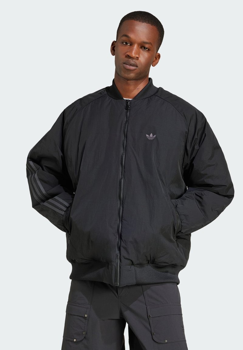 Jaqueta bomber preta com fecho de zip, punhos canelados, textura suave, apresentando um logótipo subtil e detalhes de três riscas nas mangas.