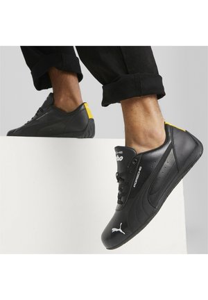 Svarta lädersneakers med låg profil, med en vit Puma-logotyp och en gul accent på hälen. Texturerad sula för grepp.