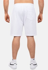 Witte katoenen shorts met een elastische tailleband, voorzien van een achterzak en een relaxed fit, gecombineerd met witte sneakers en crew socks.