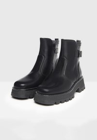 Black leather ankle boots with a chunky sole, side zipper, buckle accent, and decorative stitching around the sole for added detail.
