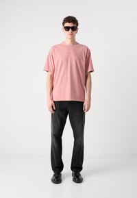 Lyserød bomulds t-shirt med korte ærmer, prydet med et lille logo på brystet. Sammen med sorte denimjeans og sorte sko.