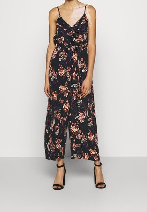 Kukkainen haalari mustasta kankaasta värikkäillä kukilla. Varustettu ohuilla olkaimilla, röyhelökauluksella ja solmittavalla vyötäröllä, yhdistetty mustiin korkokenkiin.