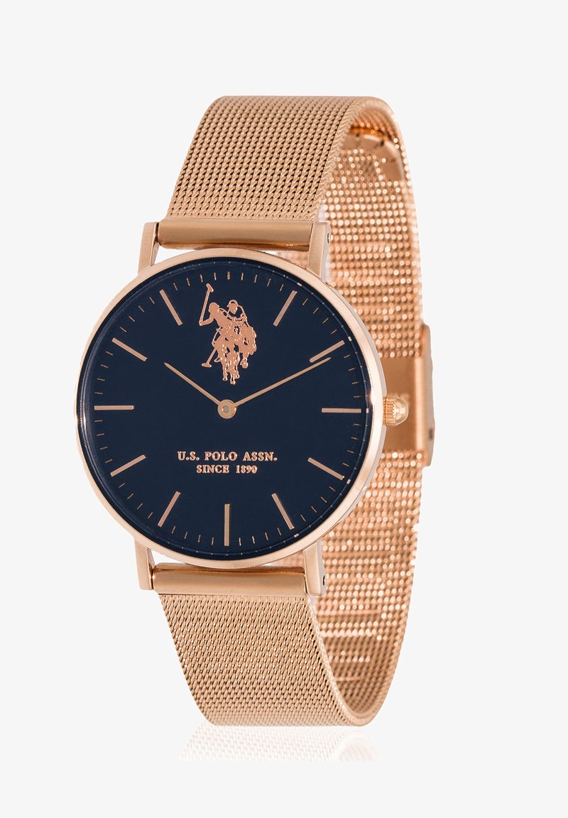 Orologio con cinturino in maglia oro rosa e quadrante blu navy, dotato di logo, marcatori delle ore minimalisti e cassa rotonda. Testo in oro.