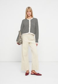Cardigan a righe bianche e nere con scollatura tonda e abbottonatura frontale; pantaloni larghi crema; borsa con stampa pitonata; ballerine bordeaux.