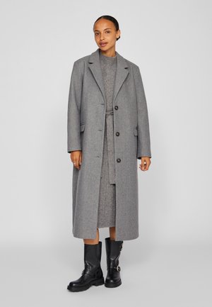 Lang grå ullfrakk med smal revers, enkeltknappet design og store knapper, lagd over et matchende grått antrekk og svarte støvler.