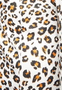 Vit tyg med oregelbundna svarta och orange leopardfläckar tryckta i ett tätt mönster.