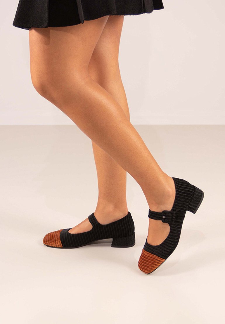 Zapatos Mary Jane de pana negra con la punta texturizada en naranja redonda, tacón bajo y un cinturón con hebilla en la parte delantera.