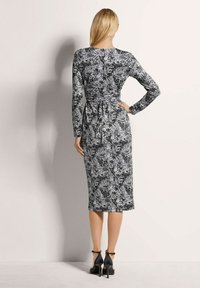 Langärmliges Schwarz-Weiß-Kleid mit einem Blatt- und Blumenmuster, tailliertem Schnitt und Midilänge. Getragen mit High Heels.