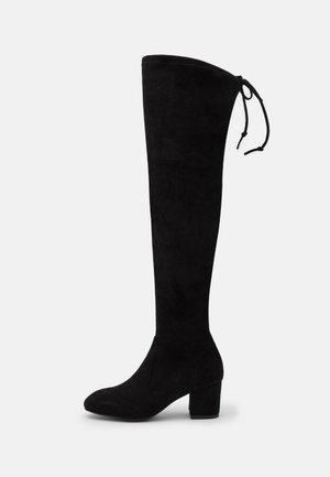Botte noire en suède hauteur genoux avec un talon carré et un détail de lacet en haut, présentée en profil latéral sur un fond uni.